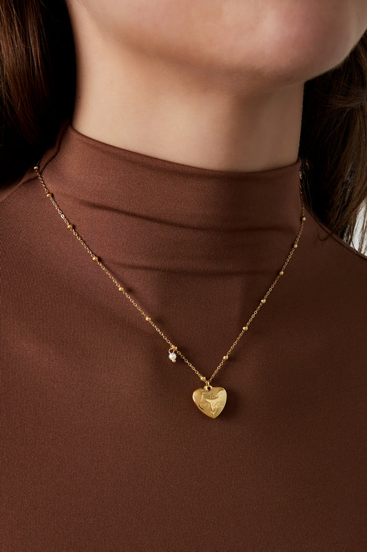 Close-up of woman wearing gold heart charm pendant necklace with brown top
