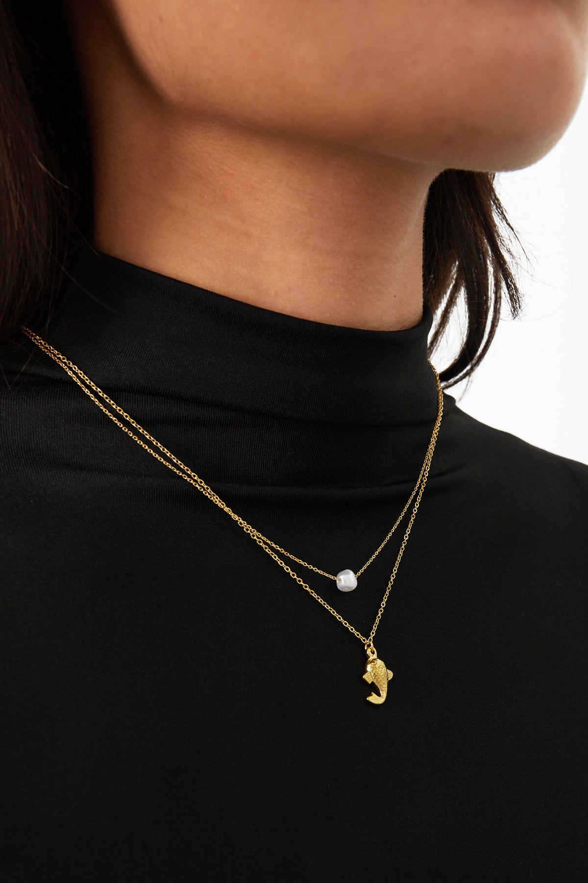 Close-up of a woman wearing the gold layered pearl and fish necklace over a black top