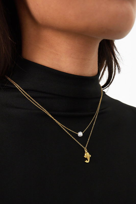 Close-up of a woman wearing the gold layered pearl and fish necklace over a black top