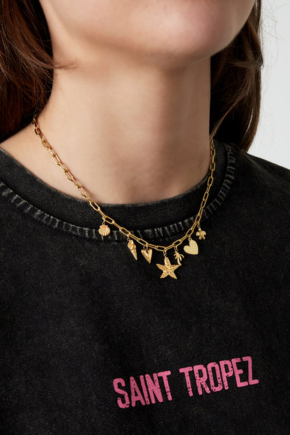 Close-up of a woman wearing a gold charm necklace with multiple beach-inspired charms, styled with a casual black top
