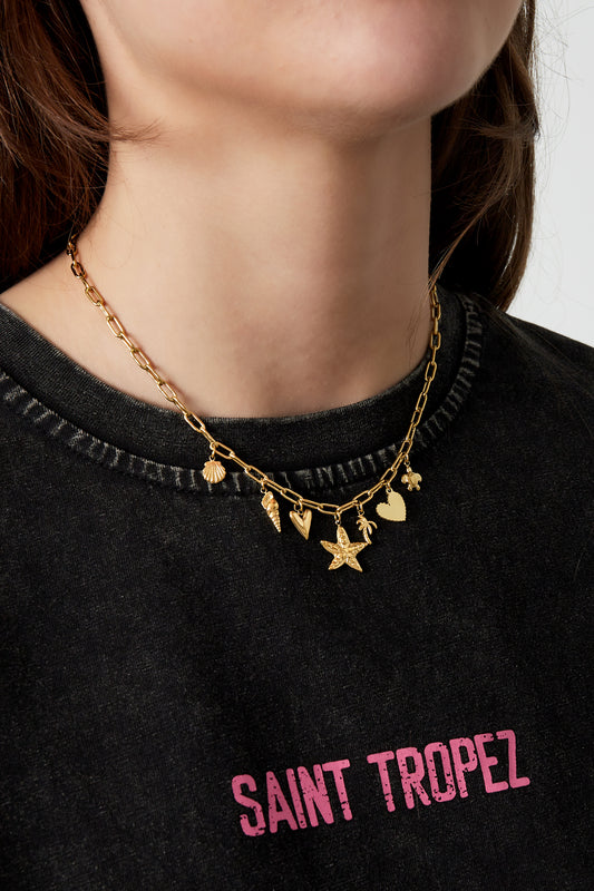 Close-up of a woman wearing a gold charm necklace with multiple beach-inspired charms, styled with a casual black top