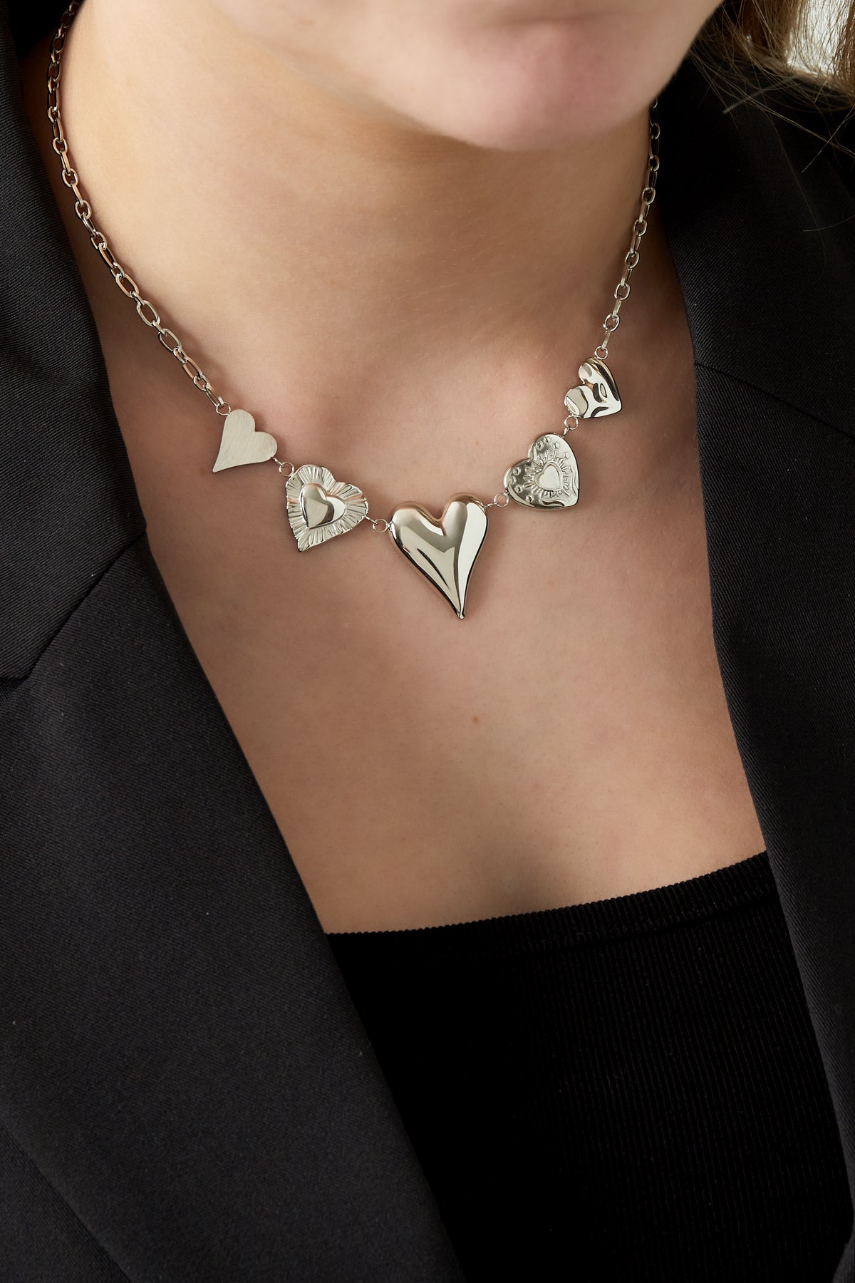 Close-up of model wearing the silver multi heart charm necklace showing detail and fit on clavicle