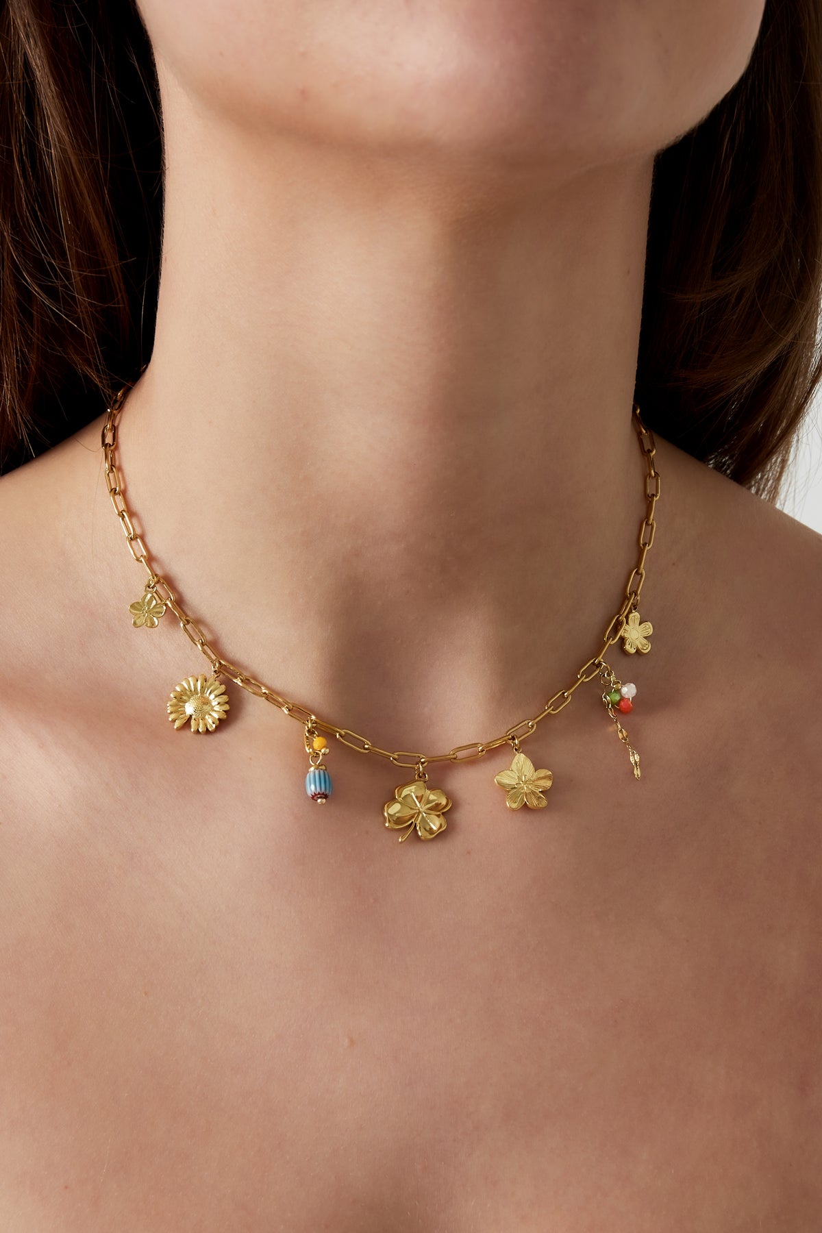 Close-up of a woman wearing the gold charm necklace showing the dainty flower and bead charms around her neck