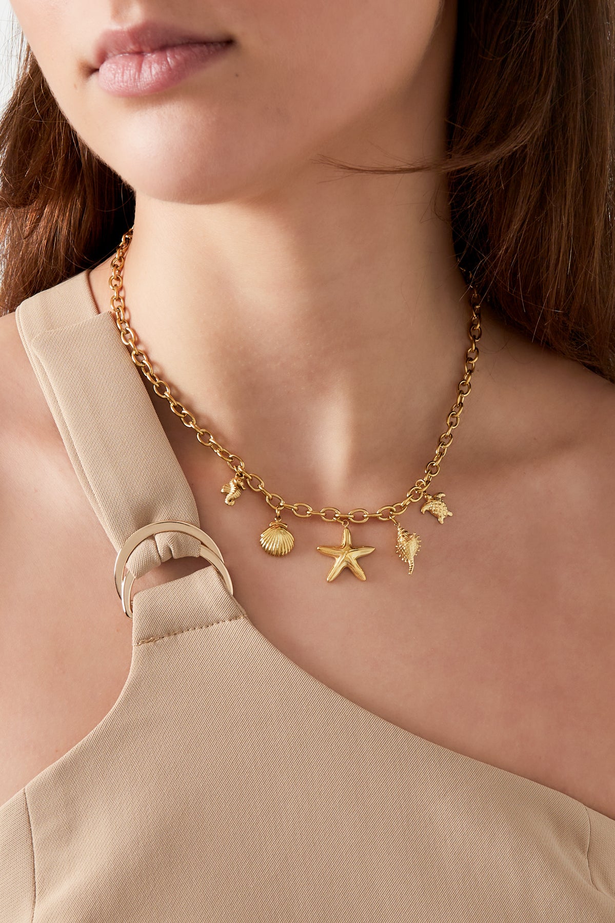 Woman wearing a gold charm necklace with beach-inspired shell and starfish charms paired with a beige sleeveless top