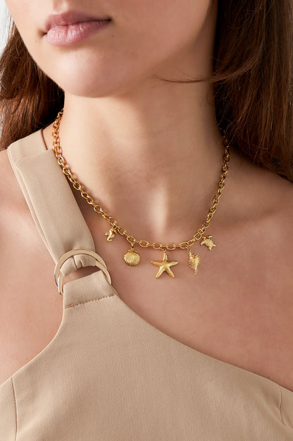 Woman wearing a gold charm necklace with beach-inspired shell and starfish charms paired with a beige sleeveless top