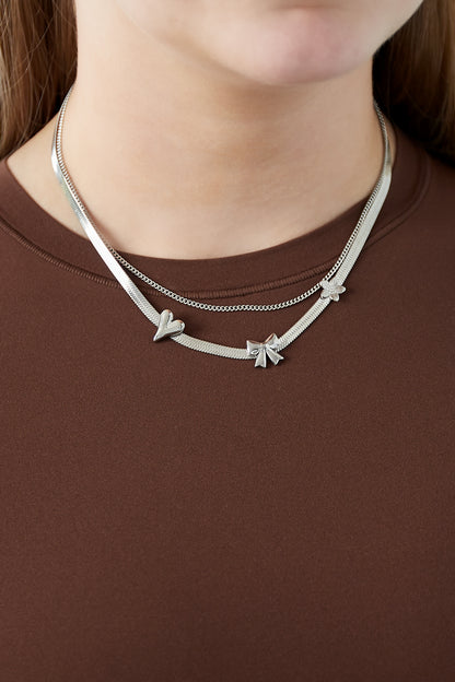 Woman wearing silver layered charm necklace with heart, bow, and flower details over brown top