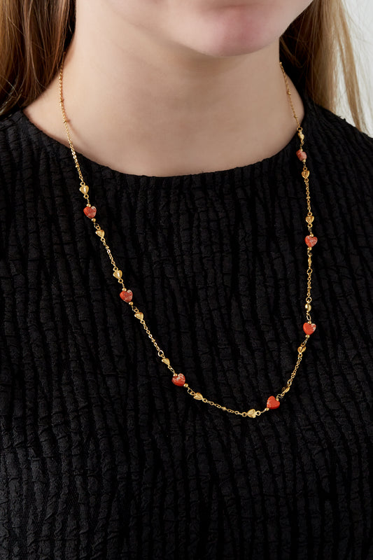 Model wearing gold-tone chain necklace with orange heart beads on black textured top
