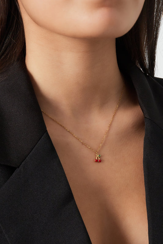Close-up of woman wearing a gold-coloured chain necklace featuring a red enamel cherry pendant, styled with a black blazer