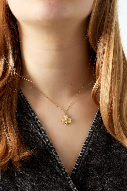 Close-up of gold clover pendant on necklace worn by woman with light brown hair and dark top