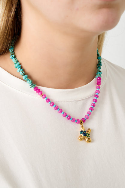 Close up of a necklace with turquoise chips, bright pink and light blue beads, and a gold letter K pendant with dark blue berry charms