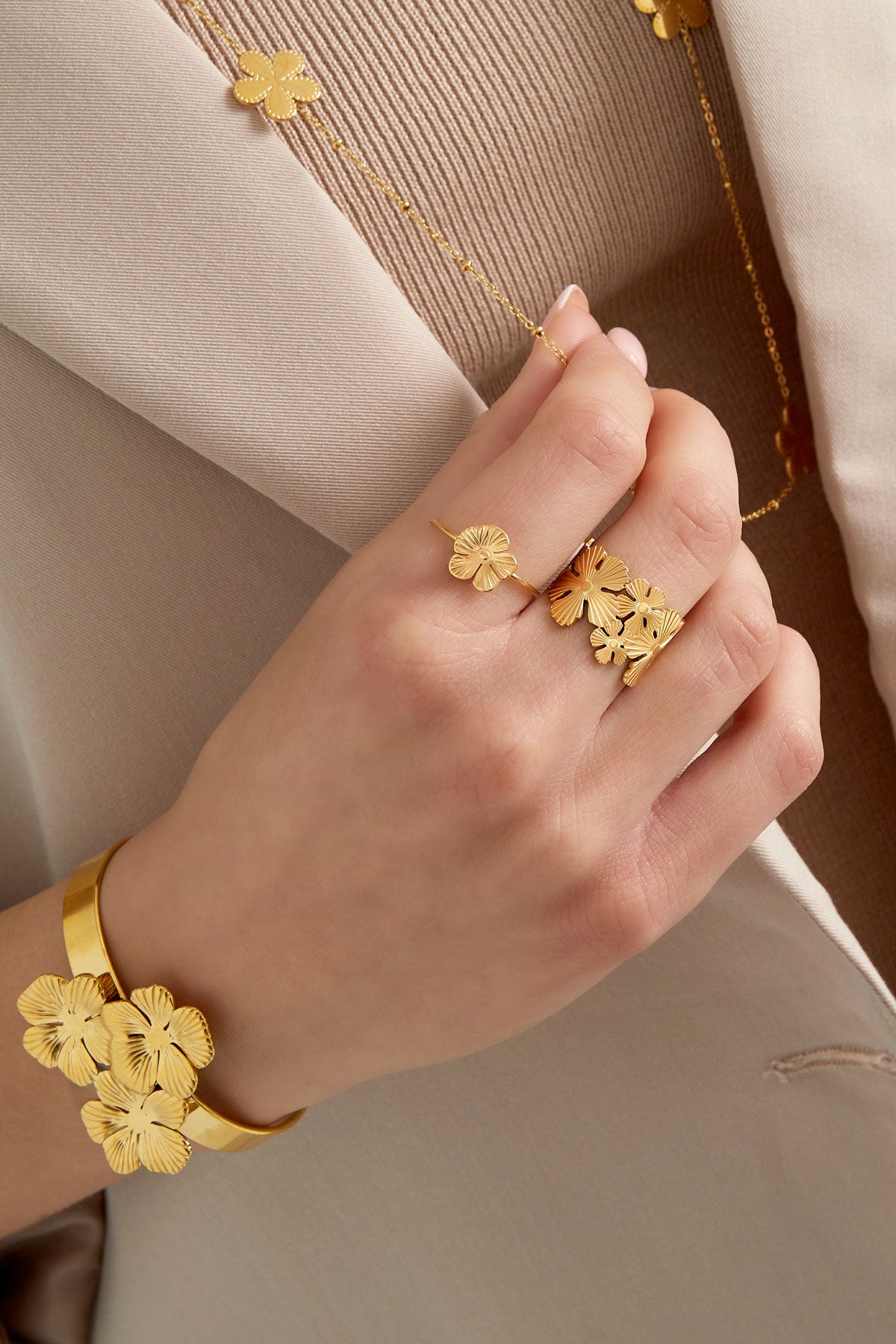 Close-up of a hand wearing a gold flower ring paired with matching floral jewelry and beige clothing