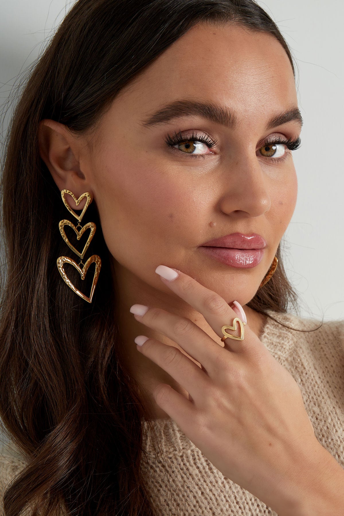 Woman wearing gold heart ring and triple heart earrings, showcasing youthful and aesthetic look