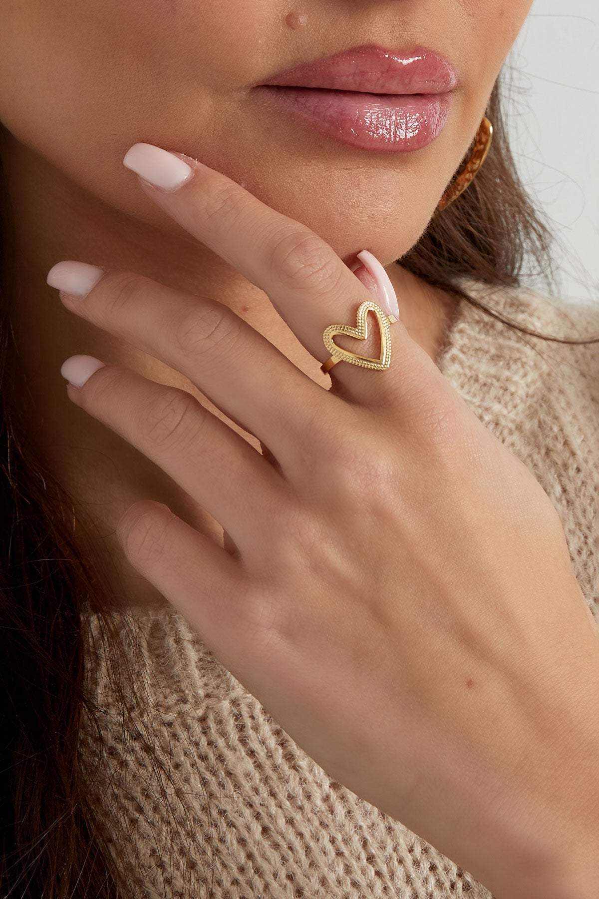 Close-up of the gold-textured heart ring worn on a woman's finger with neutral sweater