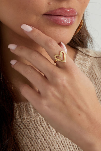 Close-up of the gold-textured heart ring worn on a woman's finger with neutral sweater