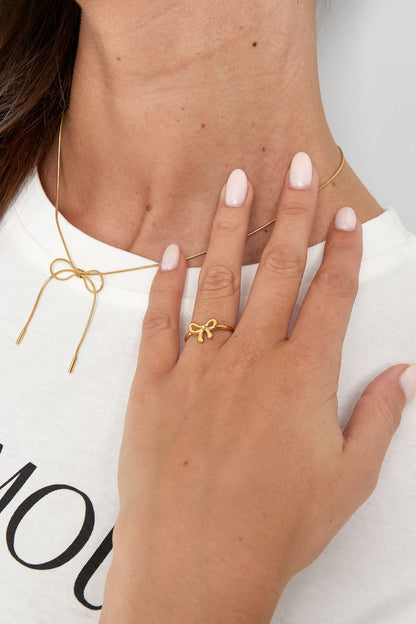 Woman wearing gold bow ring and matching bow necklace on white shirt