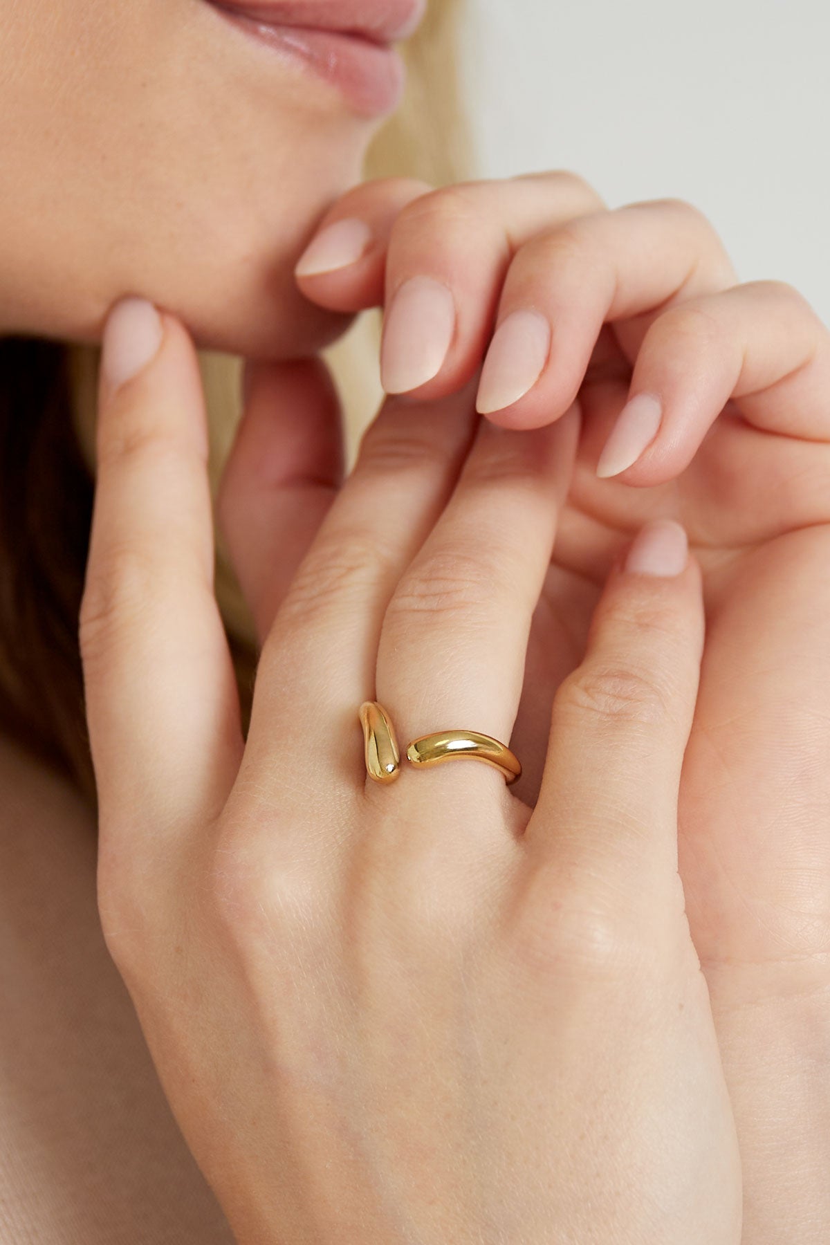 Close-up of a woman's hand wearing a gold twist open ring with a minimalist twisted design