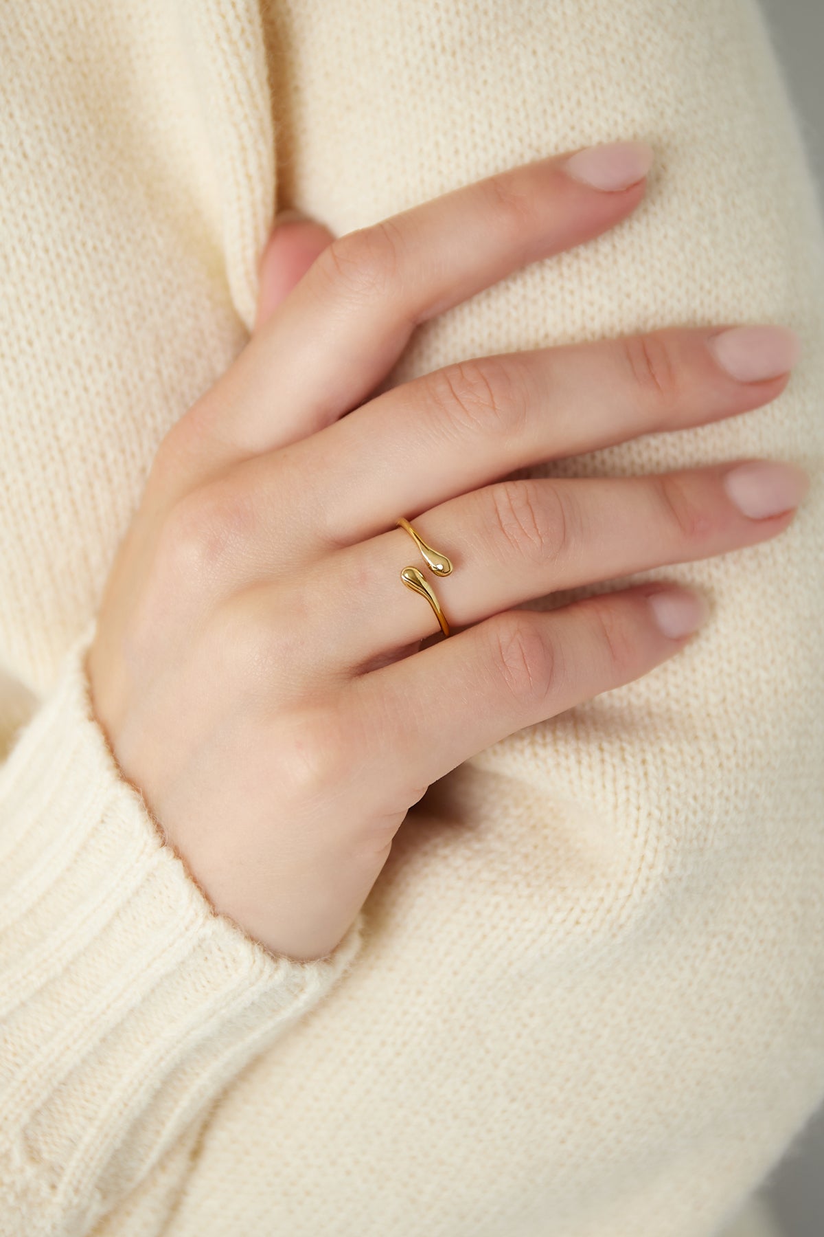 Gold open-end ring worn on a woman's hand with a cream knit sweater, showing its adjustable fit