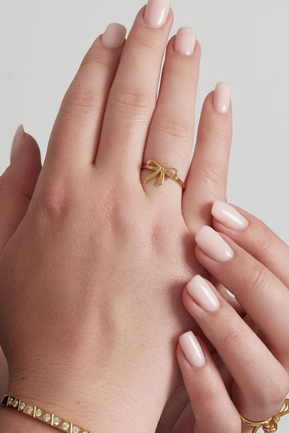 Gold bow accent ring worn on a woman's finger with neatly manicured nails