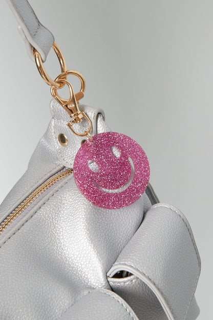 Pink glitter smiley face keychain clipped onto a silver leather handbag, highlighting gold grommets