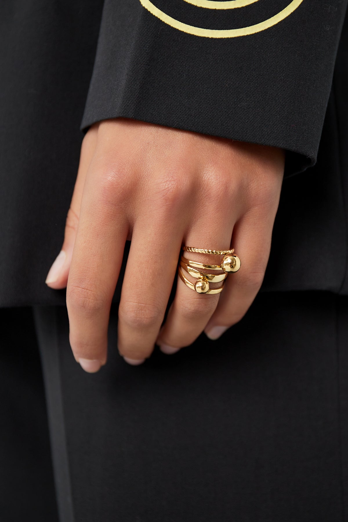 Gold layered ring worn on model's finger with black outfit showing playful chic style