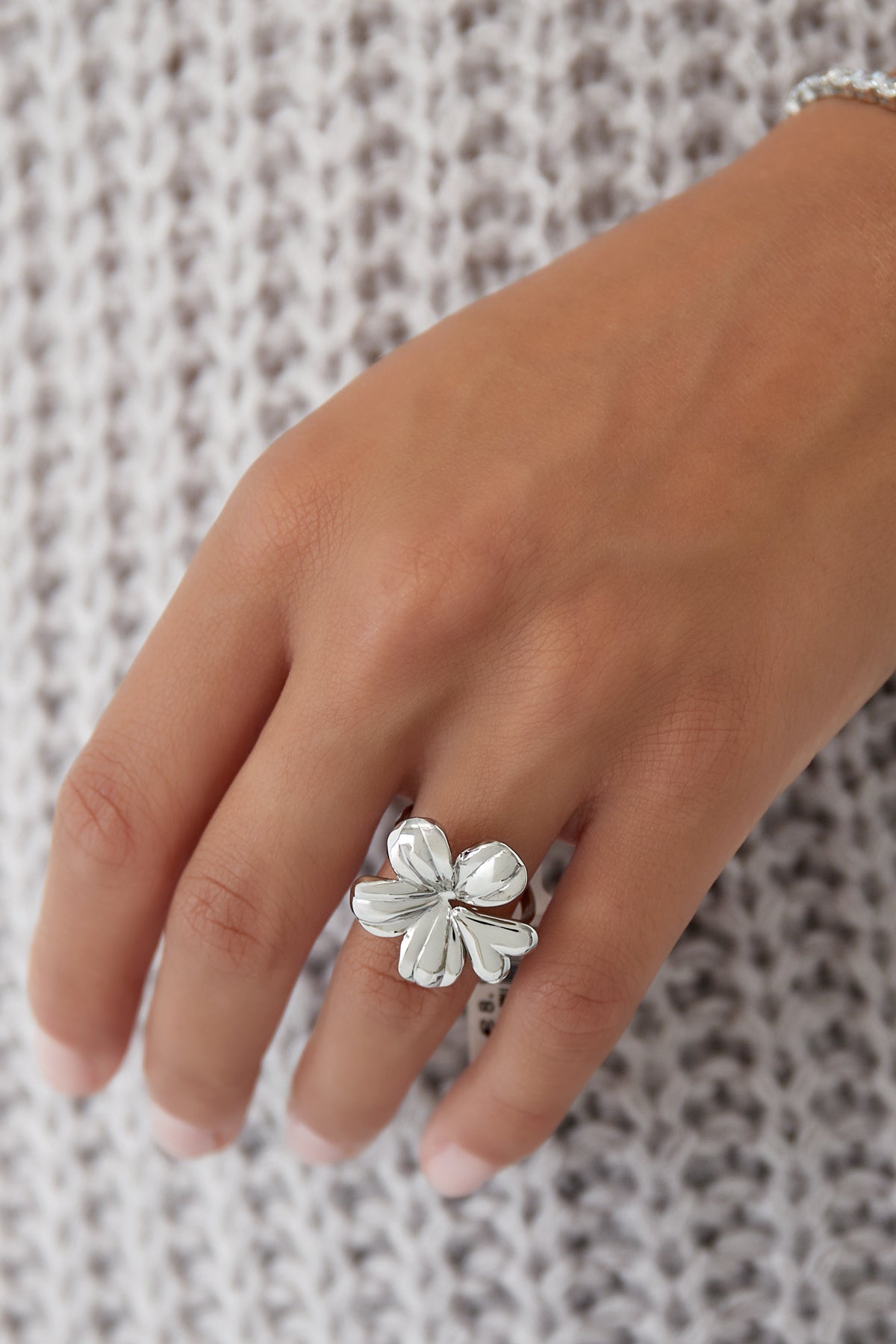 Silver floral statement ring worn on finger with knitted background