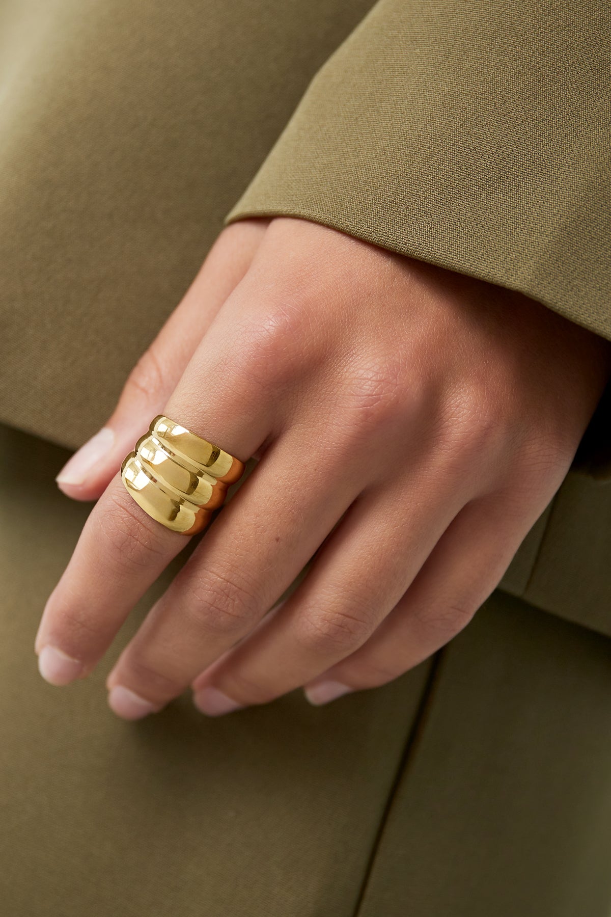 Gold three-layer statement ring worn on woman's finger with olive blazer sleeve