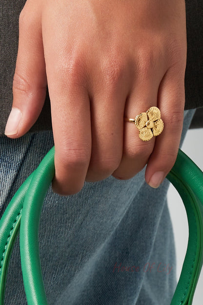 Gold textured clover ring worn on a woman’s finger holding a green handbag handle, wearing denim
