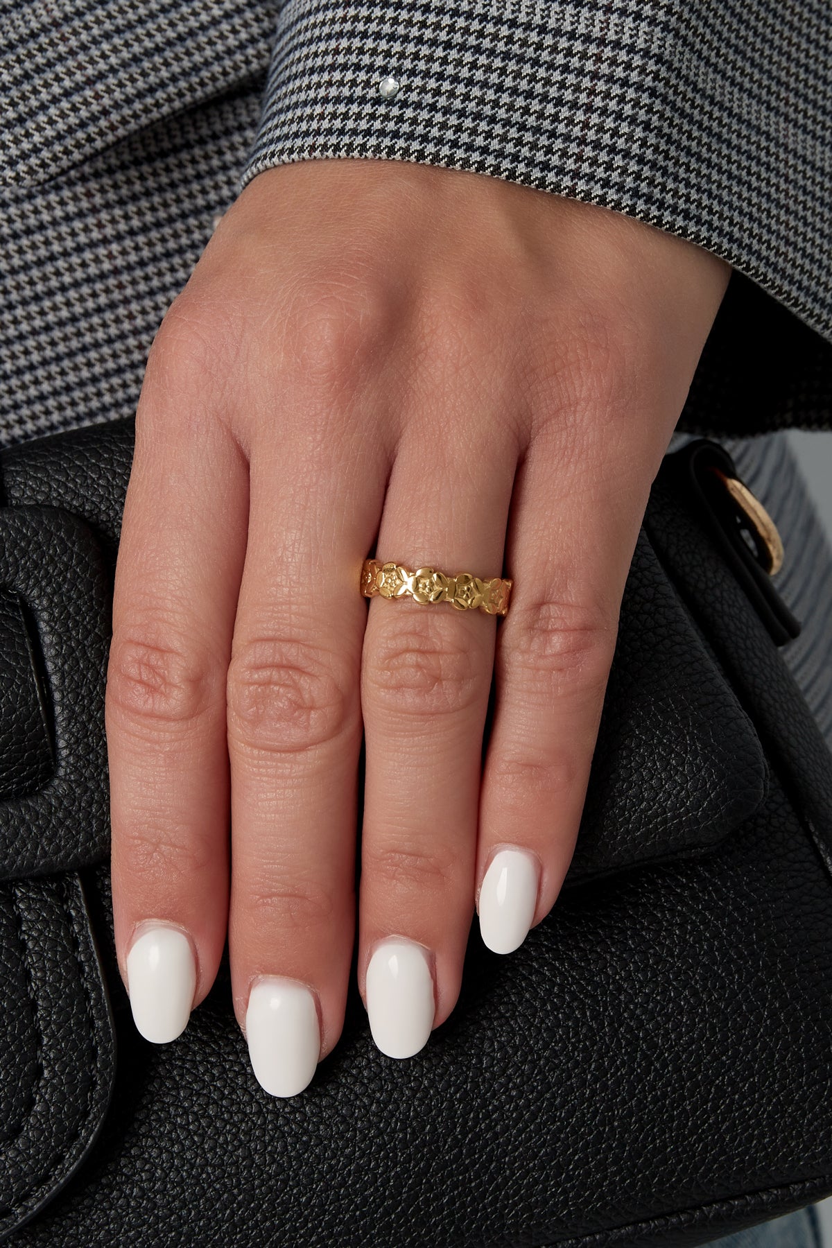 Model wearing the gold floral open band ring on the middle finger, styled with a houndstooth blazer and holding a black leather purse