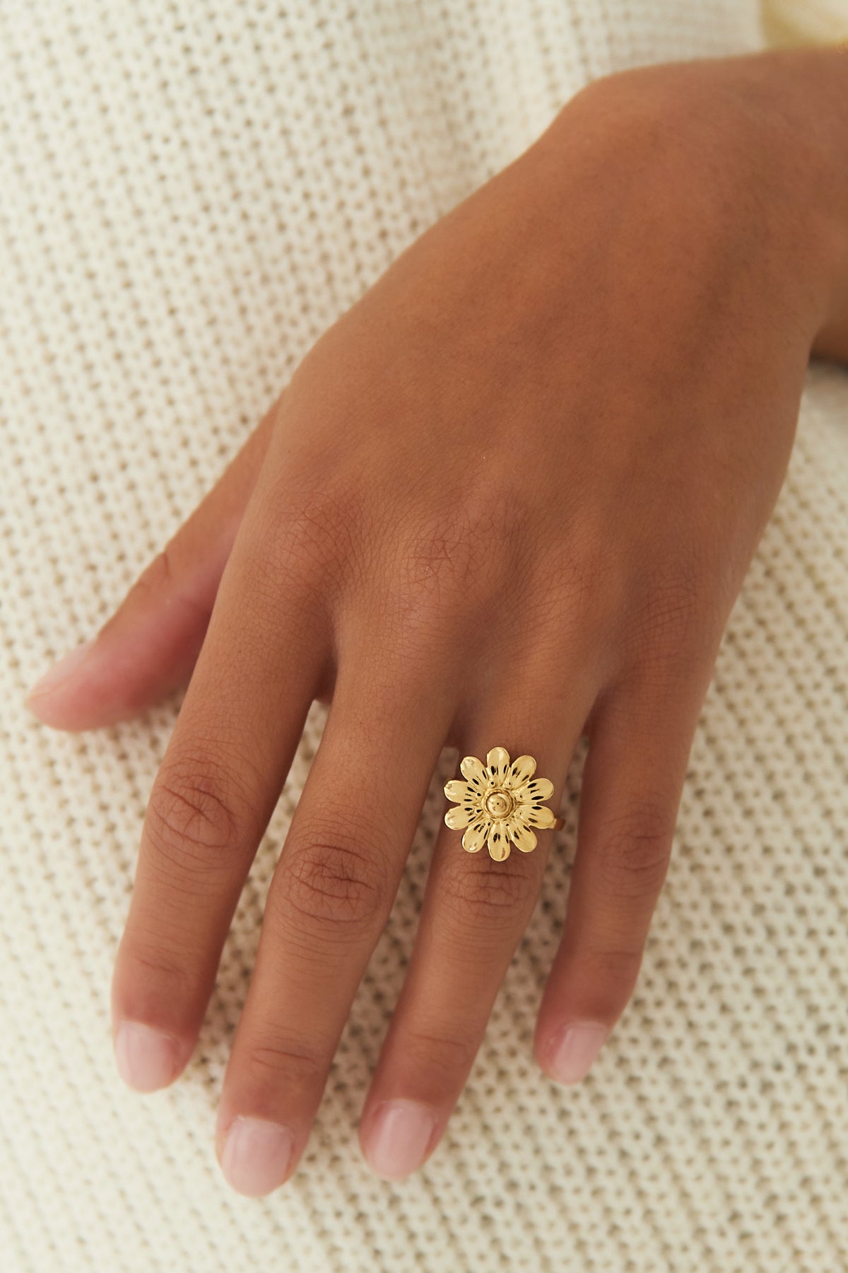 Gold daisy flower ring worn on a hand against a cream knit fabric background