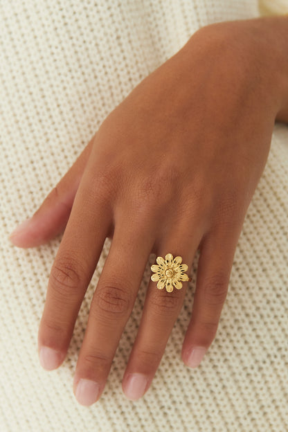 Gold daisy flower ring worn on a hand against a cream knit fabric background