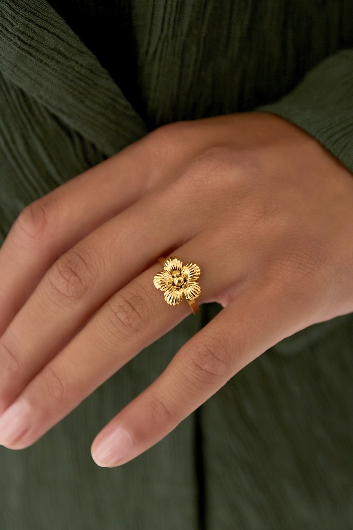 Close-up of hand wearing an adjustable gold flower ring over green fabric