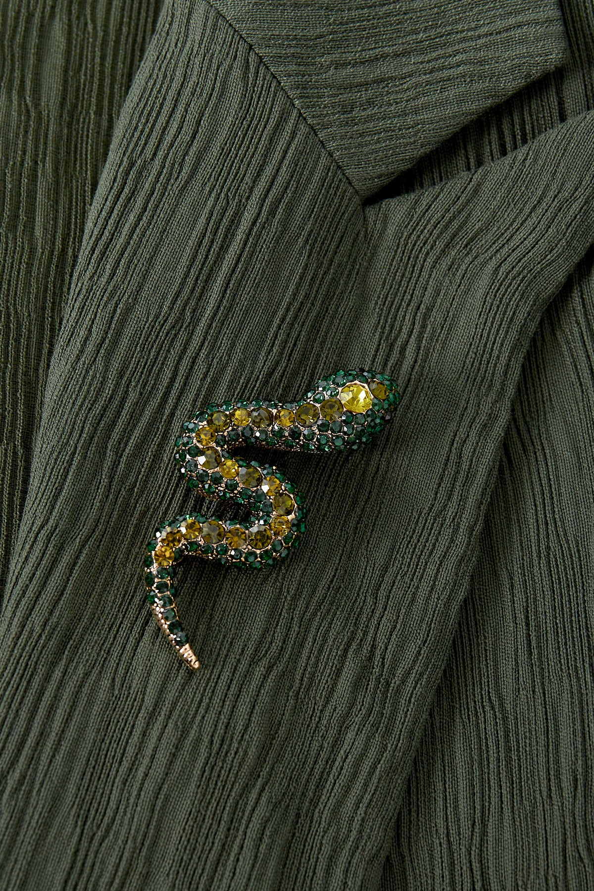 Close-up of green and yellow crystal snake brooch pinned to textured green fabric jacket