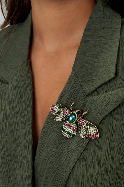 Woman wearing a green textured jacket with a gemstone bee brooch pinned on the lapel