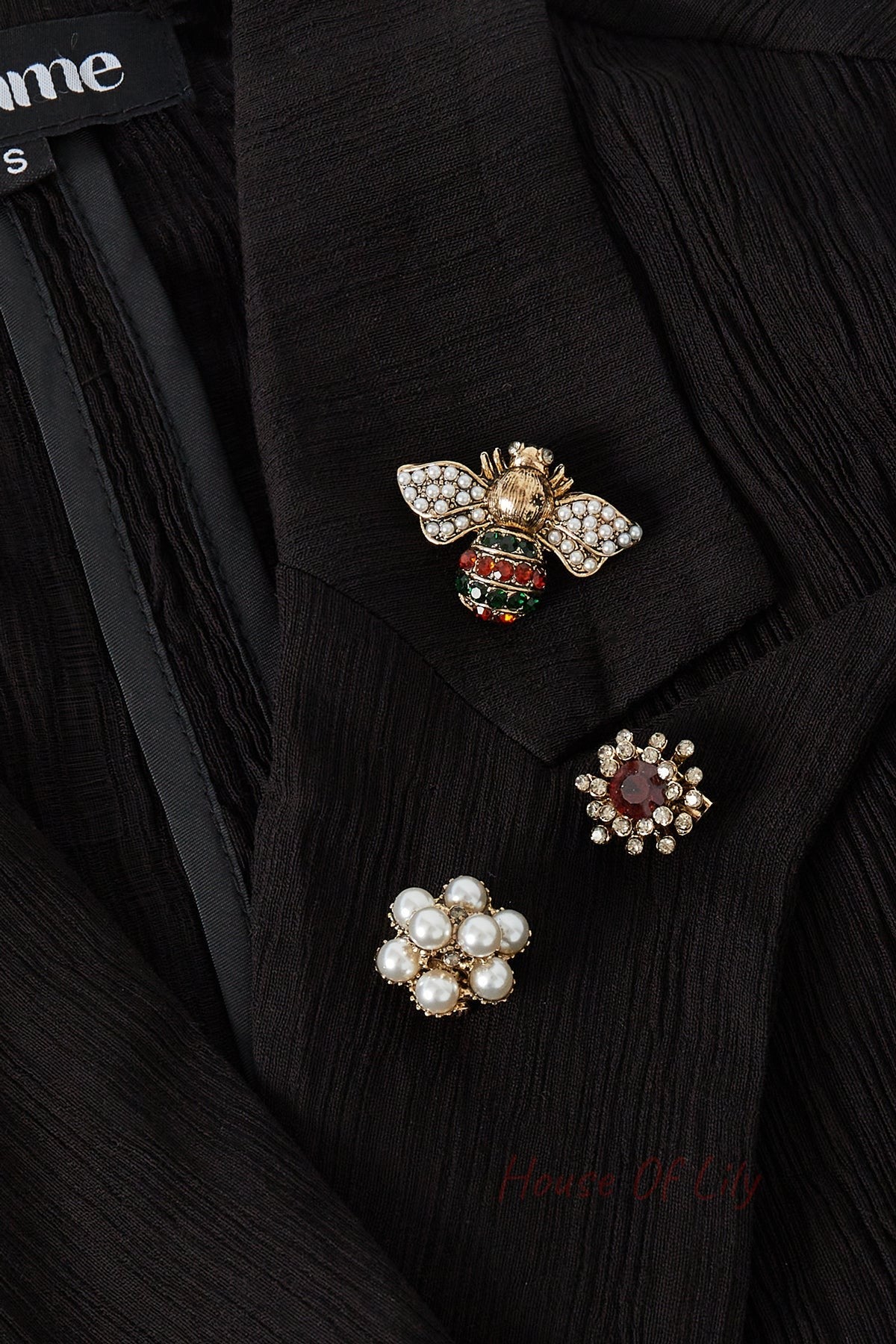 Three brooches pinned on a black blouse lapel: pearl-rhinestone bee with red and green accents, a clear red rhinestone flower, and a pearl cluster flower showcasing playful elegance