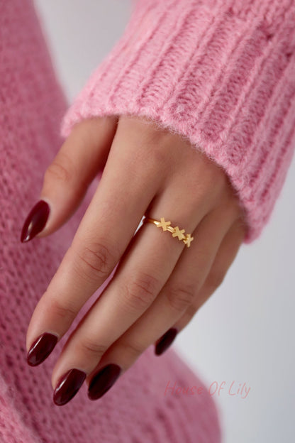 Close-up of a woman's hand wearing the gold triple cross ring with burgundy nail polish and a pink sweater