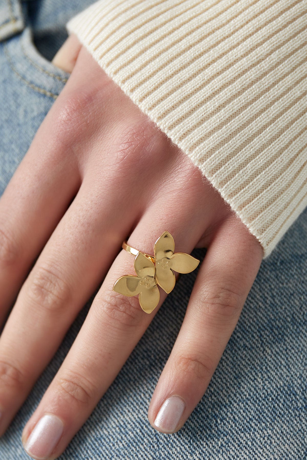 Close-up of hand wearing gold double flower statement ring with cream sweater and jeans