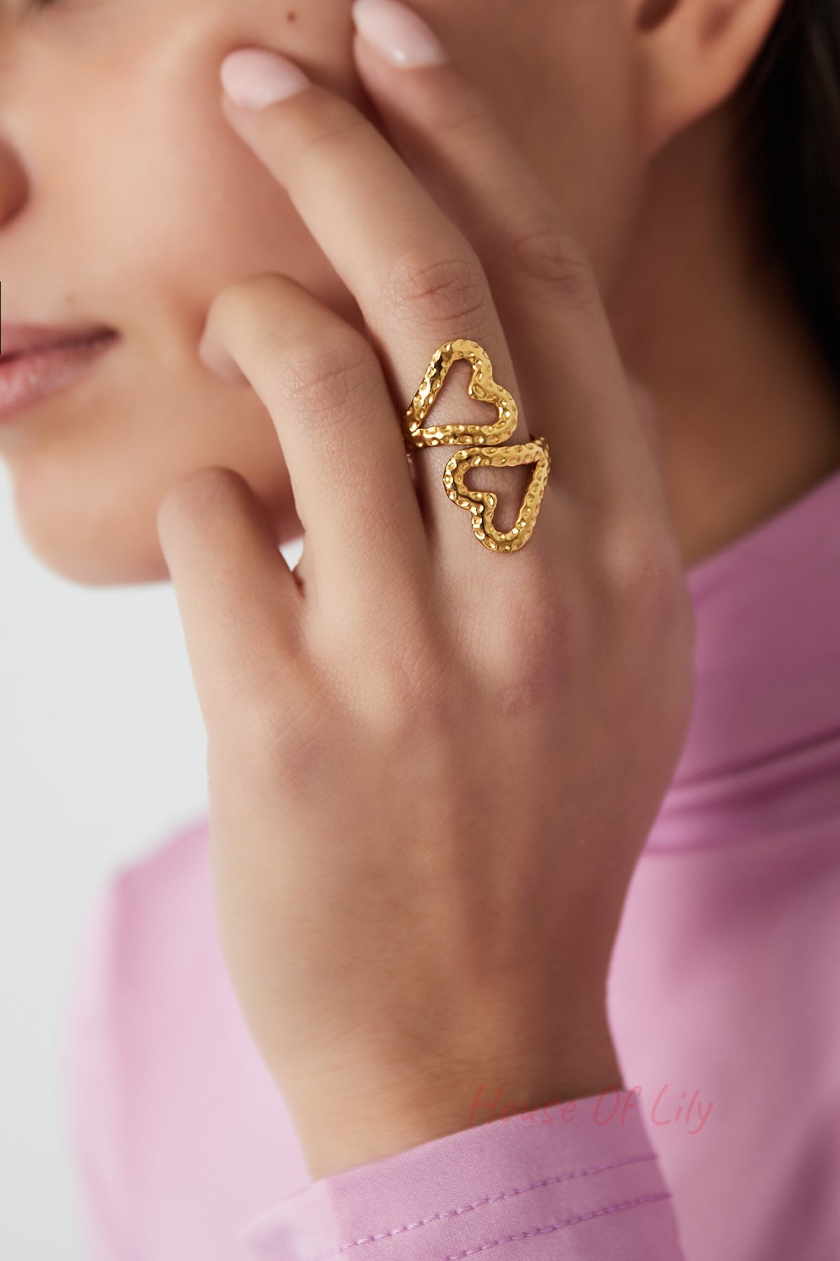 Close-up of a woman wearing the gold textured open heart ring on her finger with a pink top