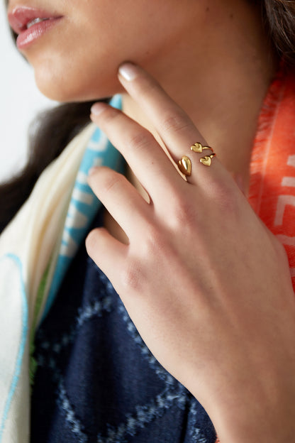 Woman wearing gold-tone trio heart open ring on finger with colorful scarf and navy clothing