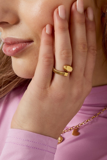 Model wearing gold coil ring on finger near her face showcasing a delicate, youthful look with a pink top