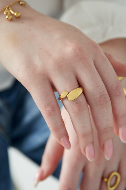 Gold-toned sculptural open ring worn on a woman's hand paired with delicate gold charm bracelet