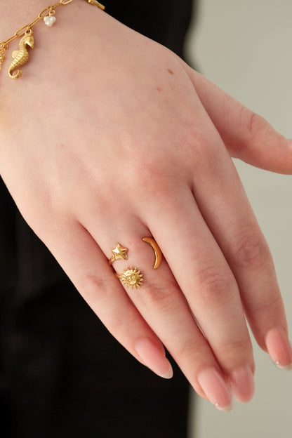 Close-up of a hand wearing a gold celestial ring featuring star, crescent moon, and sun charms