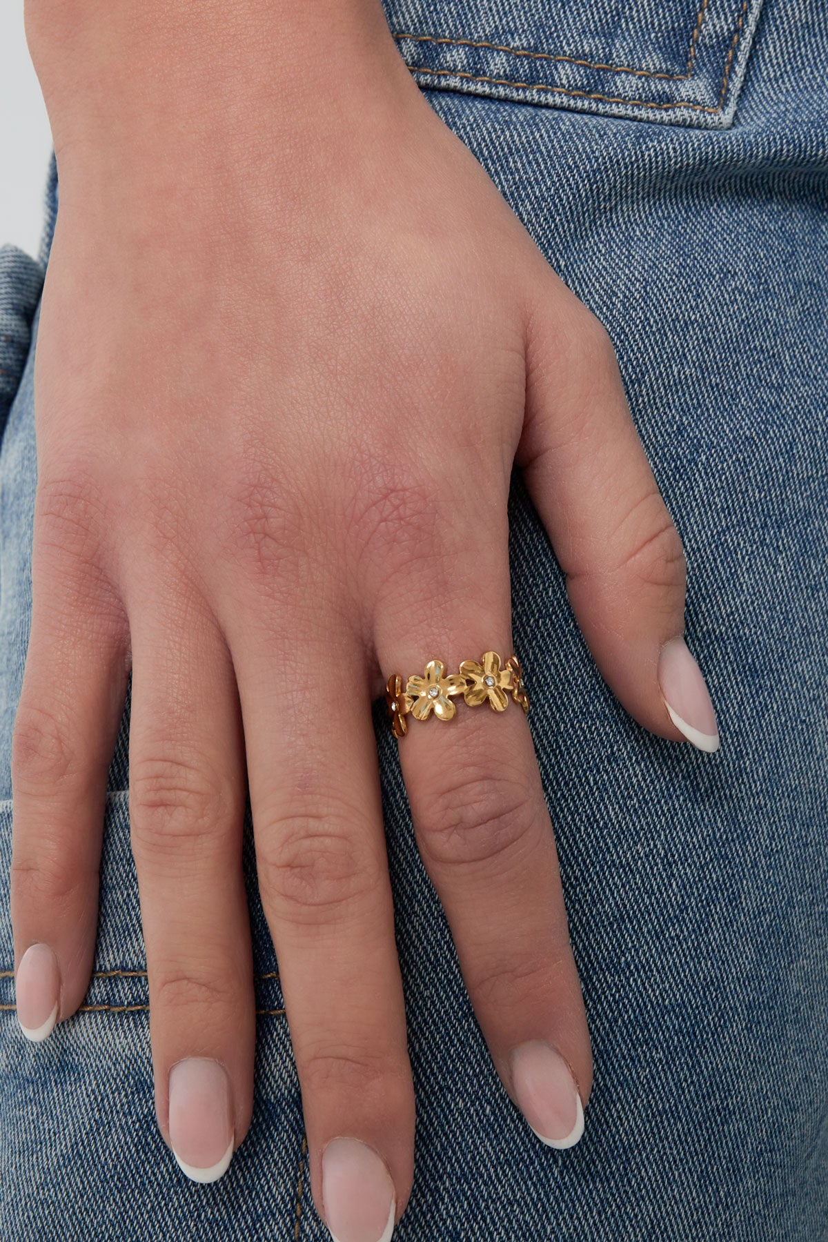 Close-up of ring worn on finger with denim jeans background, showing gold daisy design