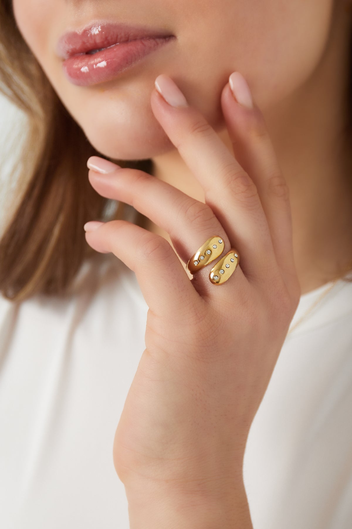 Woman wearing the gold wrap ring with crystals, gently touching her face, showcasing the ring's youthful and elegant look