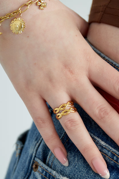 Woman's hand wearing a gold twisted double band ring paired with a sun charm bracelet and denim jeans