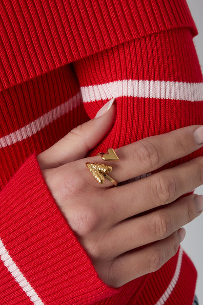 Close-up of a hand wearing the gold dual heart wrap ring paired with a red and white striped sweater