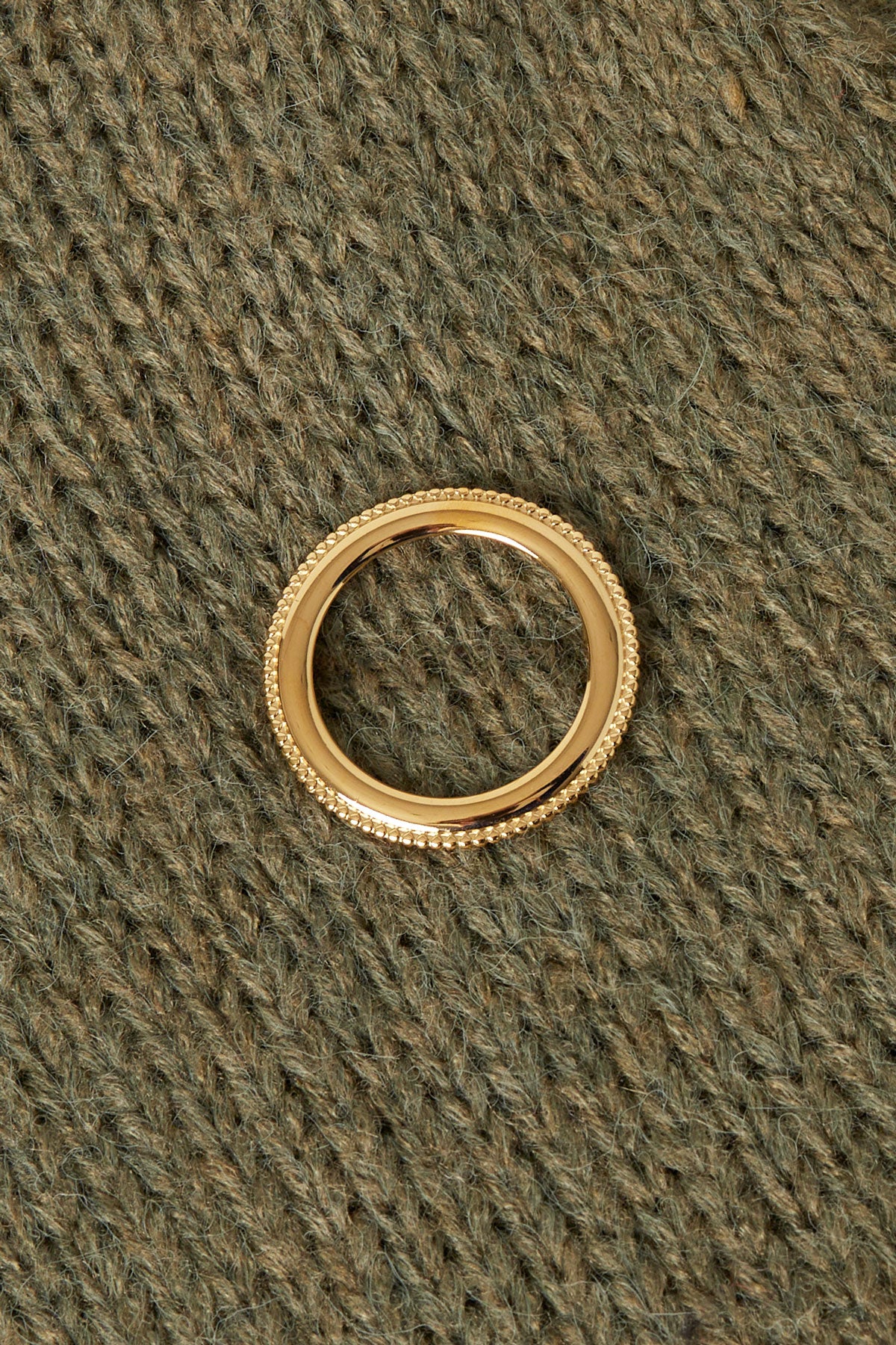 Gold circle brooch pinned on textured olive-green knitwear showcasing its minimalist, aesthetic design