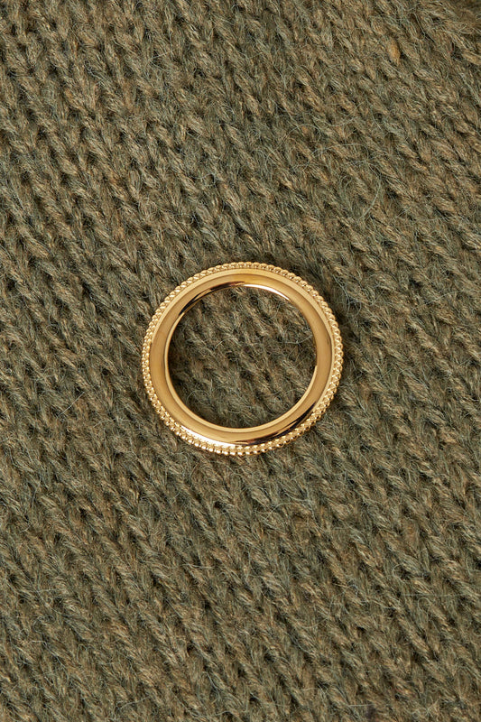 Gold circle brooch pinned on textured olive-green knitwear showcasing its minimalist, aesthetic design