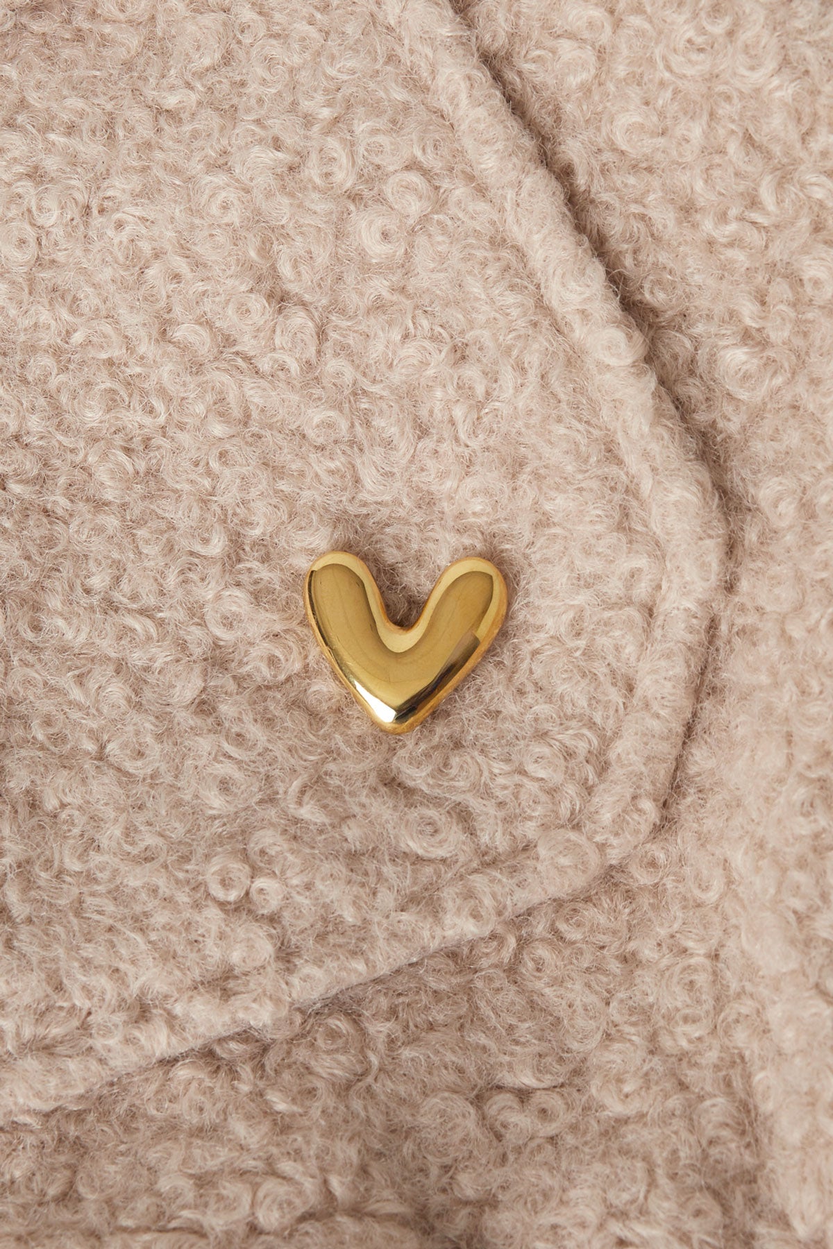 Gold heart brooch pinned onto a beige textured wool fabric, showcasing a soft and minimalistic accessory