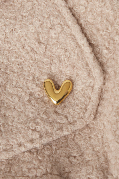 Gold heart brooch pinned onto a beige textured wool fabric, showcasing a soft and minimalistic accessory