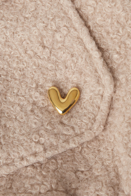 Gold heart brooch pinned onto a beige textured wool fabric, showcasing a soft and minimalistic accessory